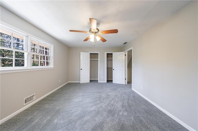 unfurnished bedroom featuring visible vents, baseboards, two closets, and carpet flooring