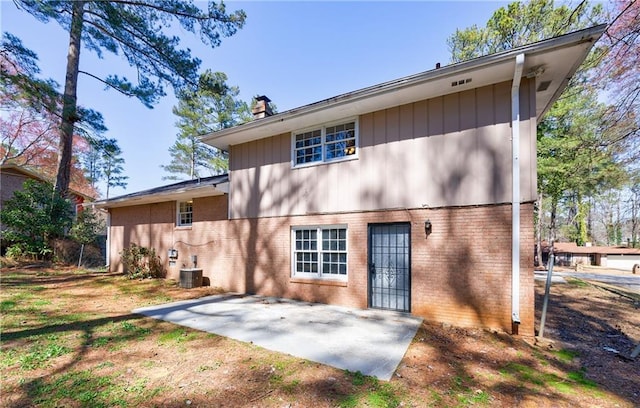 rear view of house featuring a patio area, brick siding, central AC, and a chimney