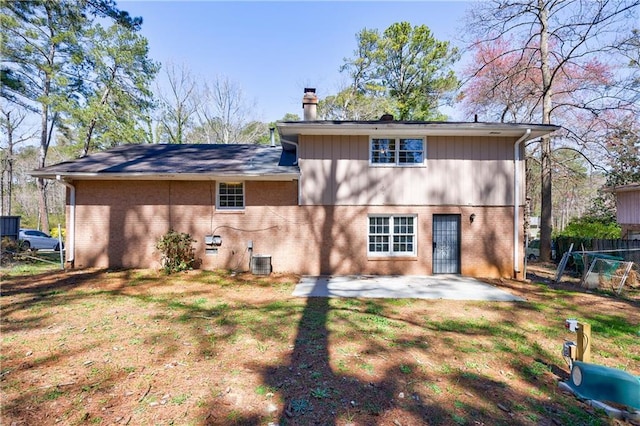 rear view of property featuring cooling unit, a patio, brick siding, and a chimney