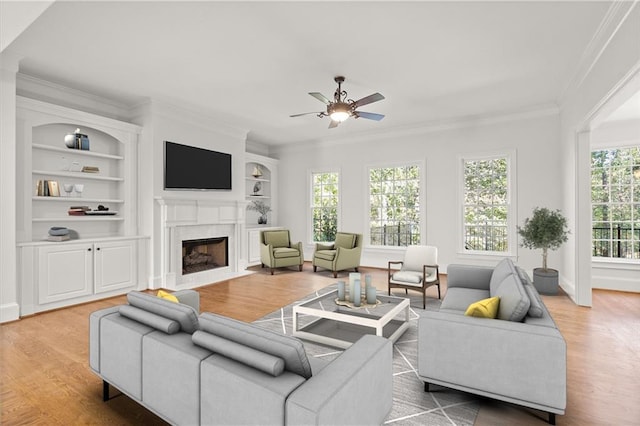 living room with ceiling fan, ornamental molding, built in shelves, and hardwood / wood-style floors