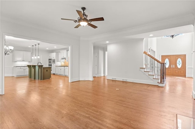 unfurnished living room with ornamental molding, ceiling fan with notable chandelier, and light wood-type flooring