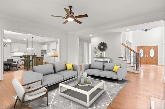 living room featuring crown molding, ceiling fan with notable chandelier, and light wood-type flooring