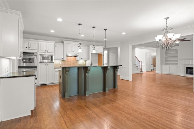 kitchen with appliances with stainless steel finishes, hanging light fixtures, white cabinetry, light hardwood / wood-style floors, and a kitchen island with sink