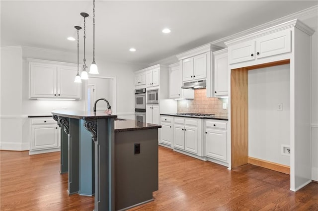 kitchen featuring white cabinets, an island with sink, appliances with stainless steel finishes, hardwood / wood-style flooring, and decorative light fixtures