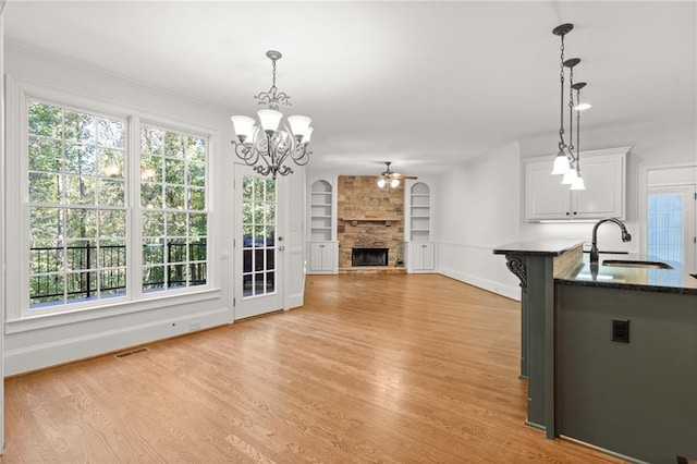 unfurnished living room featuring sink, light wood-type flooring, built in shelves, a fireplace, and ceiling fan with notable chandelier