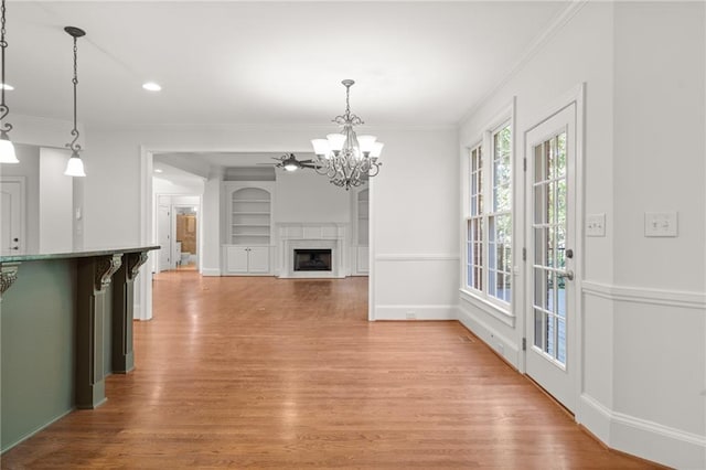 unfurnished living room with crown molding, a chandelier, light wood-type flooring, and built in shelves