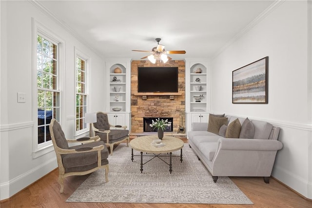 living room featuring crown molding, a stone fireplace, and light wood-type flooring