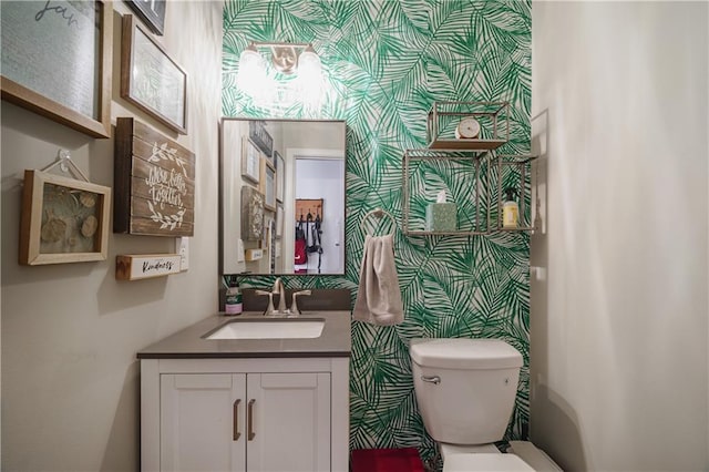 bathroom with vanity, toilet, and wallpapered walls