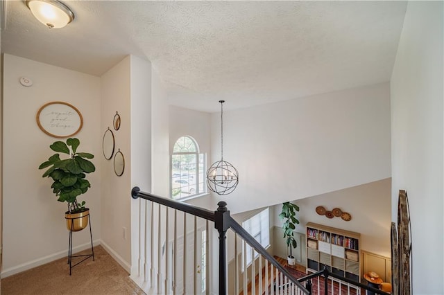 corridor with baseboards, carpet, a textured ceiling, an upstairs landing, and a chandelier