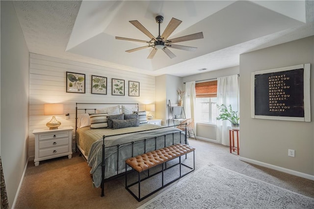 carpeted bedroom featuring a tray ceiling, wooden walls, baseboards, and a textured ceiling