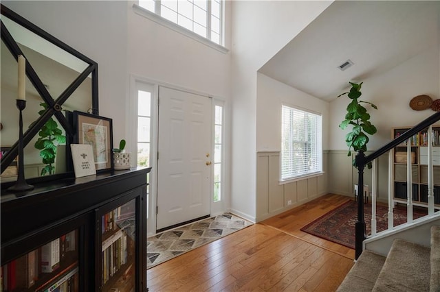 entrance foyer featuring visible vents, a towering ceiling, hardwood / wood-style flooring, a wainscoted wall, and stairway