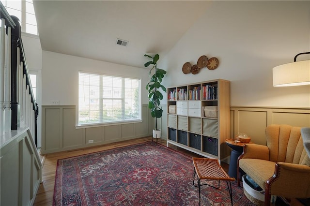 sitting room with vaulted ceiling, wood finished floors, visible vents, and a decorative wall