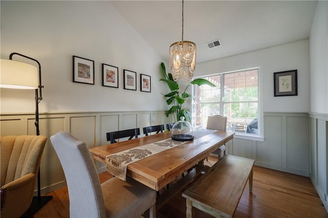 dining area with lofted ceiling, an inviting chandelier, visible vents, and wood finished floors