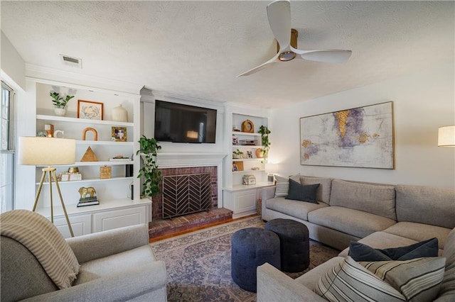 living room featuring built in features, a brick fireplace, visible vents, and a textured ceiling