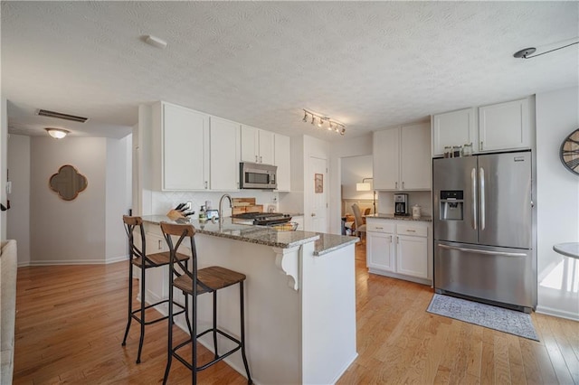 kitchen with stone countertops, a peninsula, a breakfast bar, appliances with stainless steel finishes, and light wood-type flooring