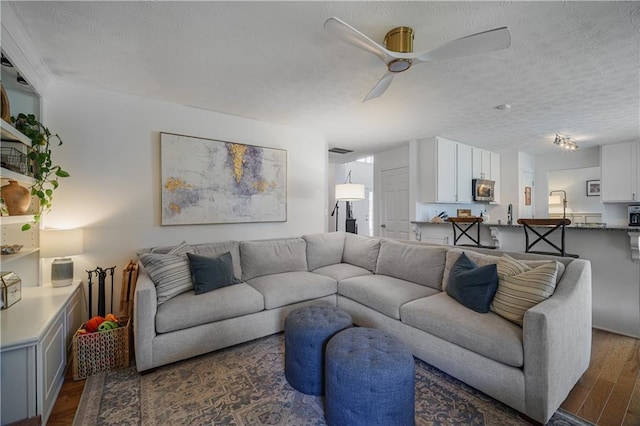 living area featuring dark wood-style floors, a ceiling fan, and a textured ceiling