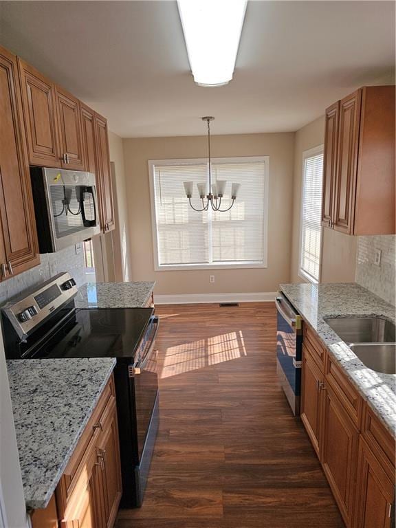 kitchen with light stone counters, hanging light fixtures, dark wood-type flooring, and appliances with stainless steel finishes