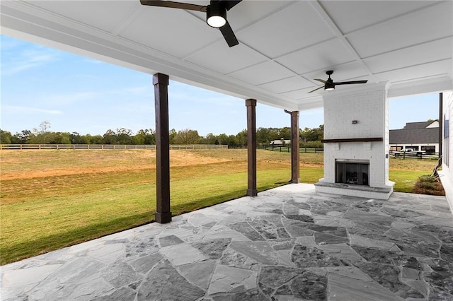 view of patio with ceiling fan, a rural view, and a fireplace