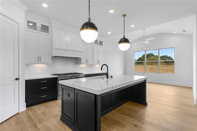 kitchen featuring white cabinets, a center island with sink, lofted ceiling, and sink