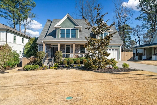 view of front facade with a garage, concrete driveway, stone siding, covered porch, and fence