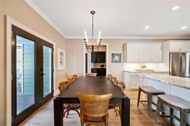 dining area with ornamental molding, french doors, light wood-style flooring, and an inviting chandelier