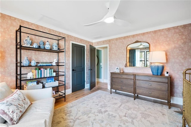 sitting room with wood finished floors, a ceiling fan, baseboards, ornamental molding, and wallpapered walls