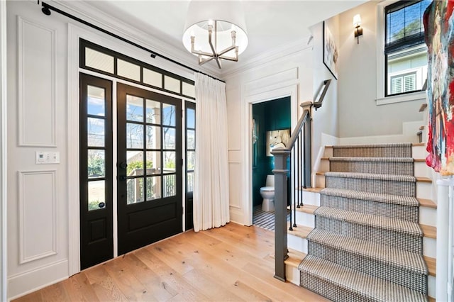 entrance foyer with light wood-style floors, crown molding, stairway, and an inviting chandelier