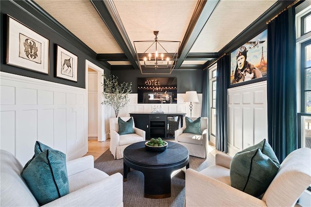 living room with a decorative wall, wainscoting, a bar, a chandelier, and beamed ceiling