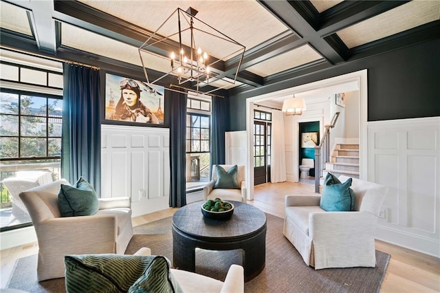 living area with a chandelier, coffered ceiling, a decorative wall, and stairway