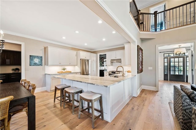 kitchen featuring under cabinet range hood, light wood-type flooring, stainless steel refrigerator, light stone countertops, and crown molding