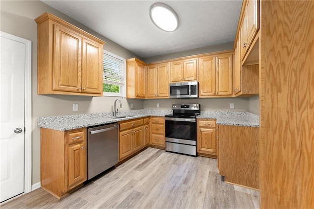 kitchen with light stone counters, sink, appliances with stainless steel finishes, and light hardwood / wood-style floors