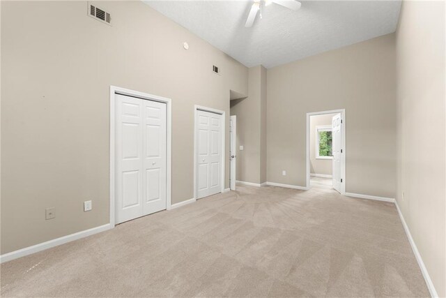 unfurnished bedroom featuring a towering ceiling, light colored carpet, multiple closets, and ceiling fan