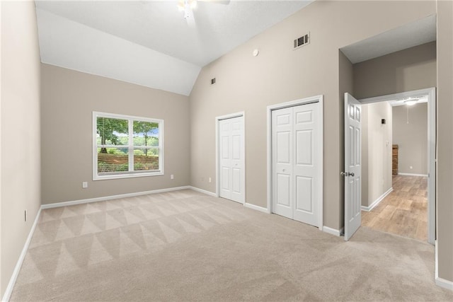 unfurnished bedroom featuring lofted ceiling, two closets, light colored carpet, and ceiling fan