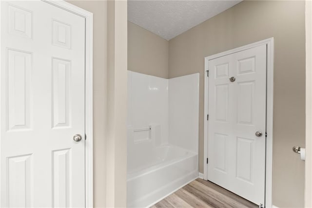 bathroom with a textured ceiling, wood-type flooring, and shower / bathtub combination