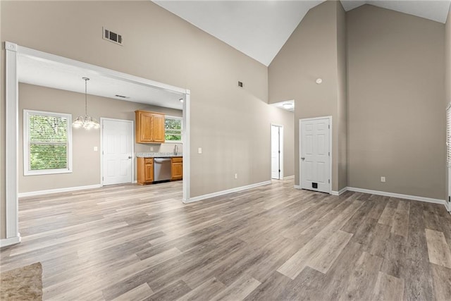 unfurnished living room featuring high vaulted ceiling, an inviting chandelier, and light hardwood / wood-style floors