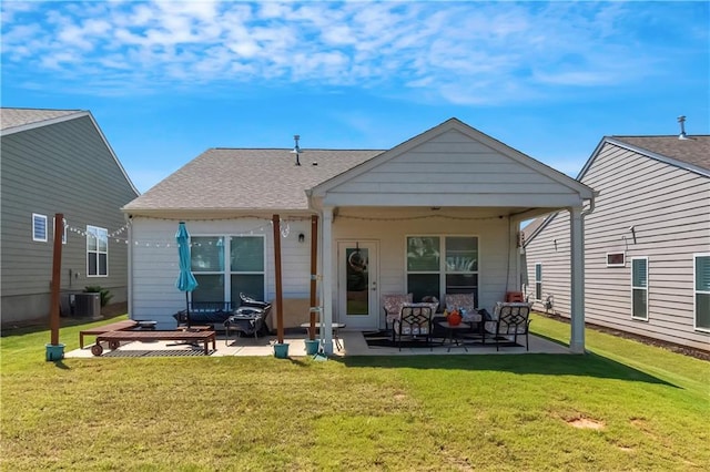 rear view of property featuring a yard, a shingled roof, central AC, and a patio