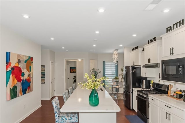 kitchen featuring under cabinet range hood, dark wood-style flooring, a kitchen island, light countertops, and appliances with stainless steel finishes