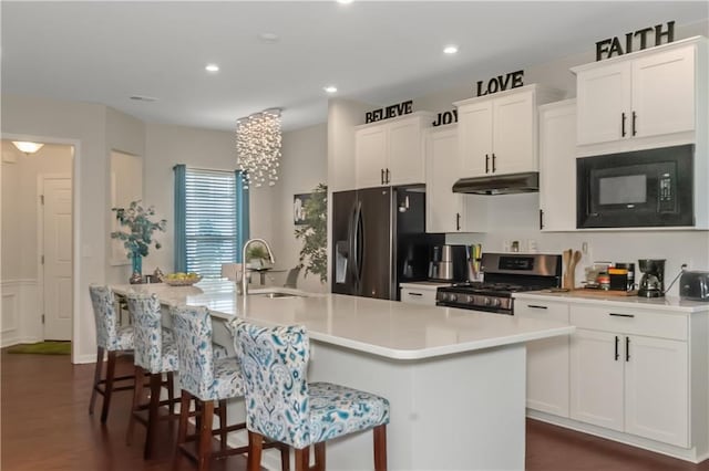 kitchen with a center island with sink, stainless steel appliances, white cabinets, a sink, and under cabinet range hood