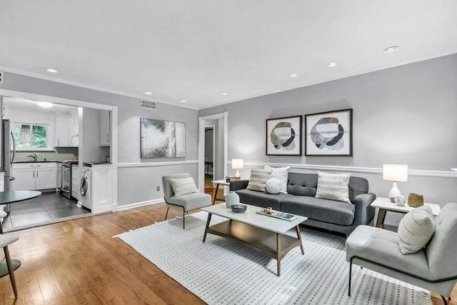 living room featuring crown molding, washer / dryer, sink, and hardwood / wood-style floors