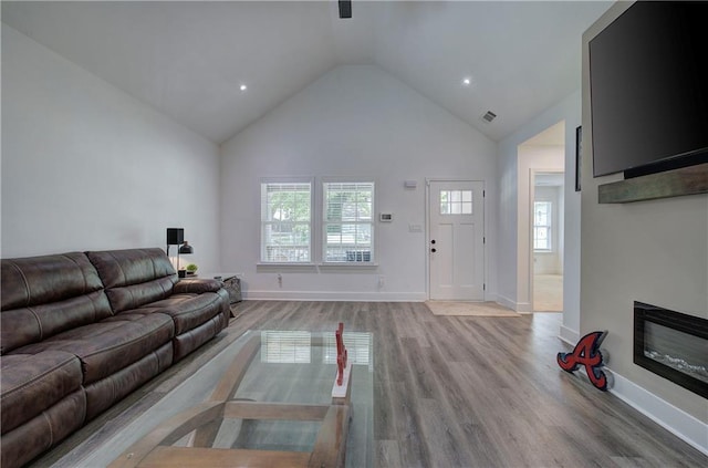 living area featuring a glass covered fireplace, visible vents, baseboards, and wood finished floors