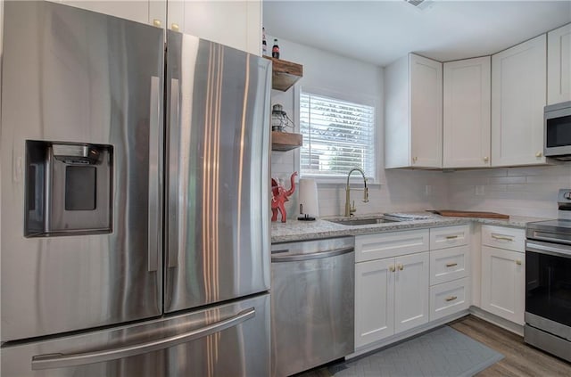 kitchen featuring stainless steel appliances, a sink, white cabinetry, and light stone countertops