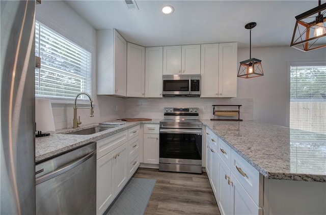 kitchen featuring light stone counters, pendant lighting, stainless steel appliances, white cabinetry, and a sink