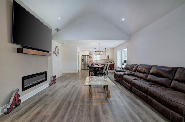 living area featuring baseboards, visible vents, a glass covered fireplace, wood finished floors, and high vaulted ceiling
