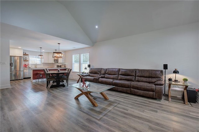 living room featuring baseboards, a chandelier, light wood-type flooring, high vaulted ceiling, and recessed lighting
