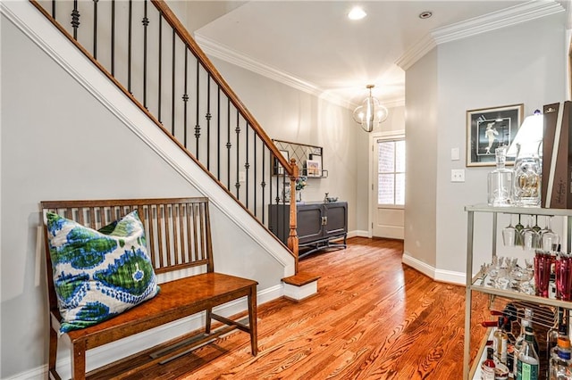 foyer entrance with crown molding, light wood finished floors, a chandelier, baseboards, and stairway
