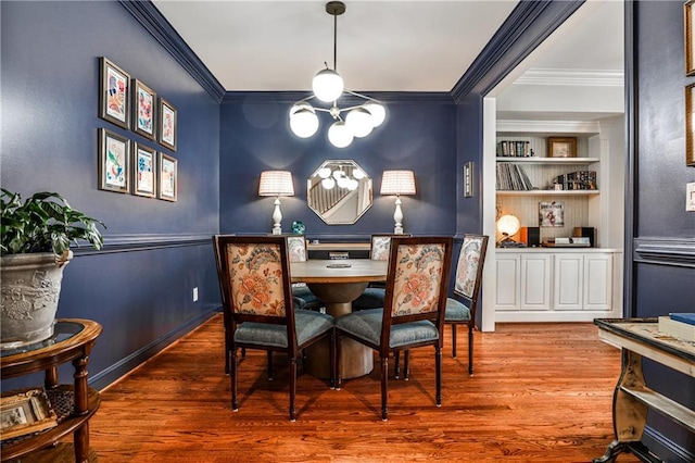 dining area featuring crown molding, a notable chandelier, built in shelves, and wood finished floors