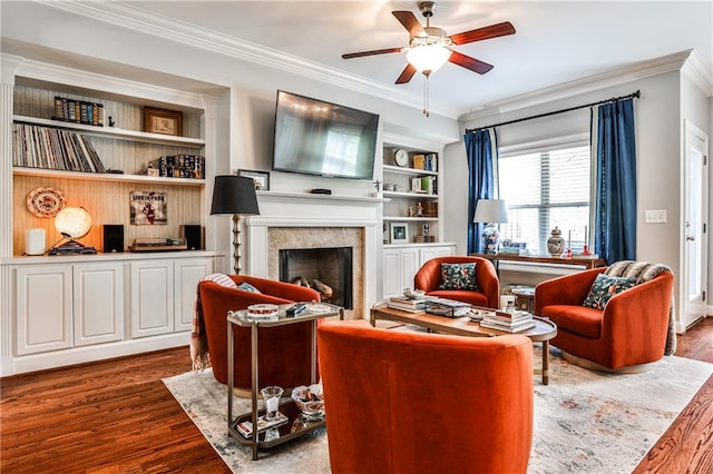 living area featuring a ceiling fan, crown molding, built in features, a fireplace, and wood finished floors
