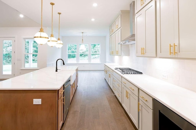 kitchen with decorative light fixtures, beverage cooler, stainless steel appliances, wall chimney exhaust hood, and a large island with sink