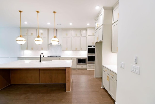 kitchen with decorative light fixtures, stainless steel appliances, light countertops, wall chimney exhaust hood, and a center island with sink