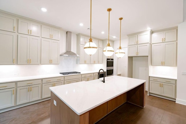 kitchen featuring decorative light fixtures, a kitchen island with sink, stainless steel appliances, light countertops, and wall chimney range hood